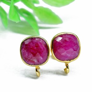 May include: A pair of gold earrings with pink gemstone square-shaped stones. The earrings have a simple design with a small loop at the bottom.