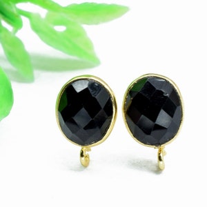 Puede incluir: Un par de pendientes ovalados negros con engastes dorados. Los pendientes tienen un diseño facetado y un pequeño bucle dorado en la parte inferior.
