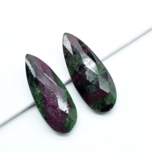 May include: Two teardrop-shaped green and purple gemstones with faceted edges.