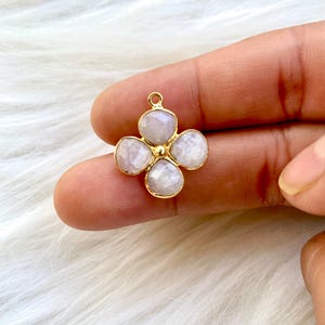 May include: A gold-tone pendant featuring a four-petal flower design with white gemstone accents.