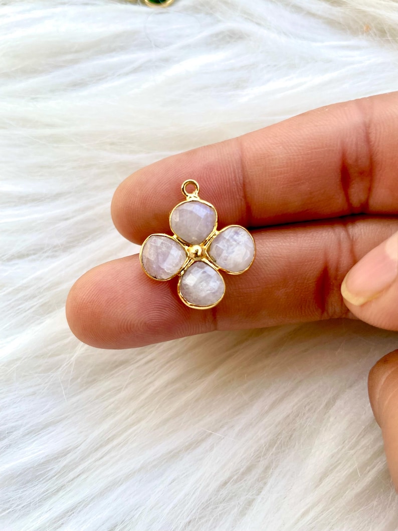 May include: A gold-tone pendant featuring a four-petal flower design with white gemstone accents.