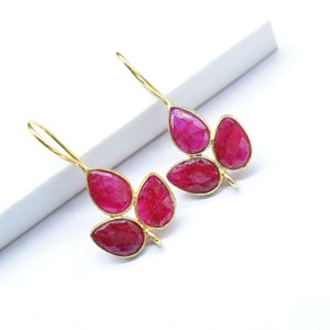 May include: A pair of gold earrings with pink gemstone drops. Each earring has three teardrop-shaped stones.