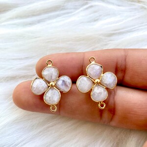 May include: Two gold-tone flower-shaped charms with a white gemstone center. Each charm has four petals and a loop for attaching to jewelry.
