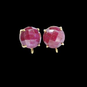 May include: A pair of ruby red gemstone earrings with gold settings. The earrings are round and have a faceted design.
