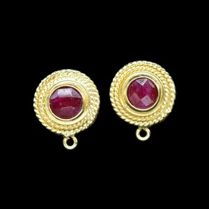 May include: A pair of gold earrings with red gemstone accents. The earrings have a round shape with a textured gold border.
