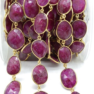 Puede incluir: Una hebra de cuentas de rub&iacute; con detalles dorados. Las cuentas son de forma ovalada y tienen un acabado facetado. La hebra est&aacute; en un recipiente transparente.