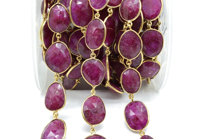 Puede incluir: Una hebra de cuentas de rub&iacute; con detalles dorados. Las cuentas son de forma ovalada y tienen un acabado facetado. La hebra est&aacute; en un recipiente transparente.