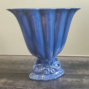 May include: A blue ceramic vase with a fluted design and a base decorated with seahorse motifs.