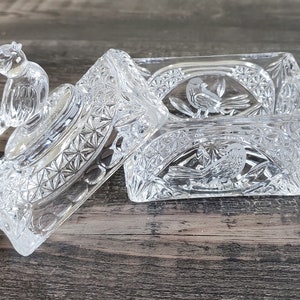 May include: A clear, rectangular glass trinket box with a lid. The lid features a small bird figurine and the box is decorated with etched bird and floral designs. The box is open, revealing the interior. The glass has a cut crystal appearance.