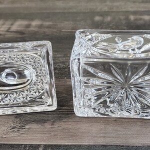 May include: A clear, rectangular crystal trinket box with a matching lid. The box and lid feature intricate starburst and floral patterns. The lid is off to the side, revealing the inside of the box.