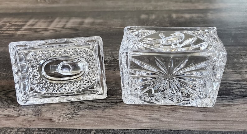 May include: A clear, rectangular crystal trinket box with a matching lid. The box and lid feature intricate starburst and floral patterns. The lid is off to the side, revealing the inside of the box.