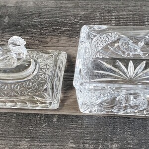 May include: A clear, rectangular crystal trinket box with a matching lid. The box and lid feature intricate cut glass patterns, including starburst and floral designs. The lid has a decorative knob.