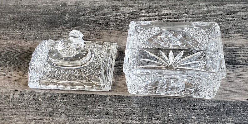 May include: A clear, rectangular crystal trinket box with a matching lid. The box and lid feature intricate cut glass patterns, including starburst and floral designs. The lid has a decorative knob.