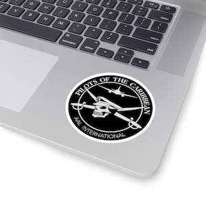May include: A black and white sticker with a skull and crossbones design. The text "Pilots of the Caribbean AAL International" is written around the skull and crossbones.