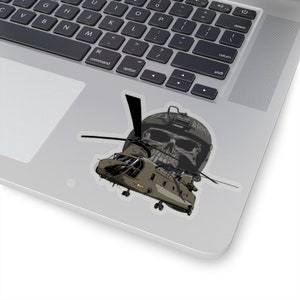 Op de afbeelding: Een sticker met een militair helikopterontwerp met een schedelafbeelding. De helikopter is olijfgroen en zwart, met een schedel met een helm erachter. Het woord "ARMY" is zichtbaar op de helm.