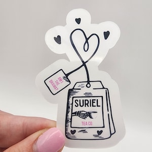 May include: A black and white tea bag sticker with a heart-shaped string and the text "Suriel Tea Co." and "Am I the drama?"  The sticker has a skeleton hand holding a teacup.