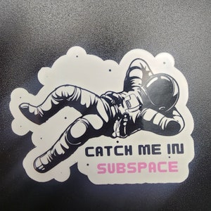 May include: A black and white illustration of an astronaut floating in space with the text "Catch me in subspace" in black and pink.