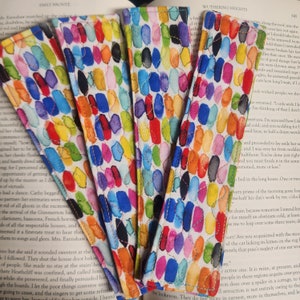 May include: A collection of colorful fabric bookmarks with a repeating pattern of oval shapes in various colors. The bookmarks are made of fabric and have a quilted design.