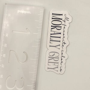 May include: A white sticker with black text that reads "My favorite color is MORALLY GREY".