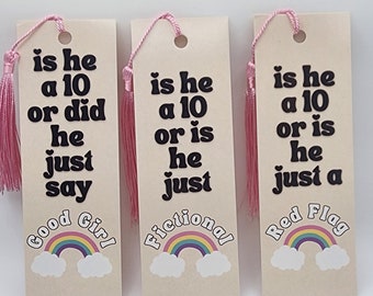 Puede incluir: Tres marcapáginas beige con borlas rosas y diseños de arcoíris. El texto en los marcapáginas dice "is he a 10 or did he just say Good Girl", "is he a 10 or is he just Fictional", y "is he a 10 or is he just a Red Flag".
