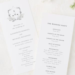 May include: Two white wedding programs with black text and floral details. One program reads "Welcome to the wedding of Katherine Kendall and Michael Reynolds" with the date and location. The other lists the wedding party. White flowers are scattered around.