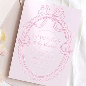 May include: Pink baby shower invitation with a delicate lace design and a large bow. The invitation reads "Please join us for Charlotte's Baby Shower".