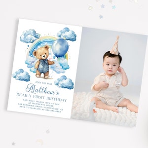 May include: A blue and white invitation for a first birthday party with a teddy bear holding a blue balloon and a rainbow in the background. The invitation says "Join us for Matthew's Bear-y First Birthday".