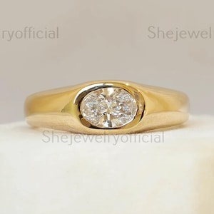 May include: A gold ring with an oval-shaped, clear gemstone set in the center. The ring is displayed on a white, textured surface. The words "Shejewelryofficial" are repeated around the image.