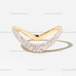 May include: A curved gold ring featuring a V-shaped band adorned with a pavé setting of numerous small, clear, sparkling stones along the front surface. The polished gold metal creates a smooth, continuous arc that tapers toward the ends.