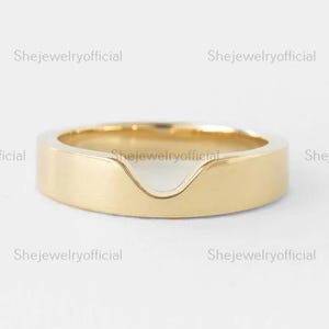 May include: A gold-colored ring with a unique V-shaped design. The ring has a smooth, polished finish and a flat band. The ring is a piece of jewelry.