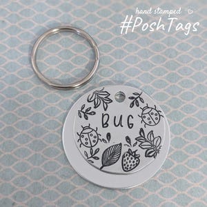 May include: Silver key chain with a round tag that says "Bug" and has a ladybug, leaves, and a strawberry design.