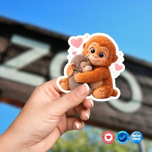 May include: A die-cut sticker featuring a large, fluffy orange monkey hugging a smaller, grey, sleeping baby monkey. The design includes several small pink hearts floating around the monkeys, all set against a white border outline.