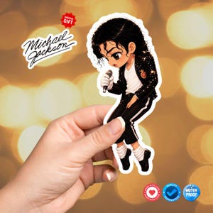 May include: A sticker featuring a cartoon illustration of Michael Jackson in a black sequined jacket, white shirt, and black pants. The sticker includes the text "Michael Jackson" and a "Special Gift" label. The sticker is held in a hand.