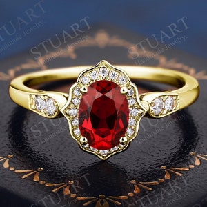 Può includere: Un anello di fidanzamento in oro con una grande pietra di rubino ovale circondata da un alone di diamanti più piccoli. L'anello è incastonato in un delicato design a filigrana.