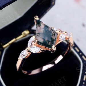 Peut inclure: Une bague en or rose avec une pierre précieuse en agate mousse verte en forme de cerf-volant. La bague est sertie de petites pierres précieuses claires sur la bande. La bague est dans un écrin à bague bleu.