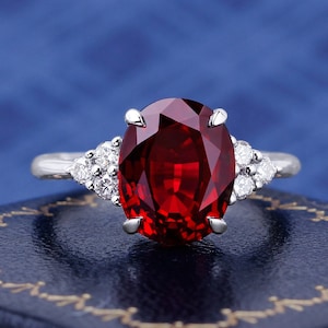 May include: A silver ring with a large oval-shaped red gemstone surrounded by smaller white gemstones.