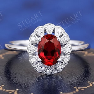 Pode incluir: Um anel de prata com uma grande gema vermelha ovalada cercada por um halo de diamantes menores.