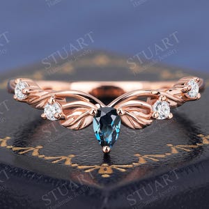 May include: A rose gold ring with a delicate, leafy design. The ring features a pear-shaped blue topaz gemstone in the centre, surrounded by smaller diamonds.
