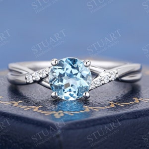 Può includere: Un delicato anello d'argento con una pietra preziosa di topazio blu rotonda e una fascia intrecciata accentuata da piccoli diamanti.
