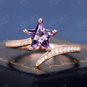 May include: A rose gold ring with a purple star-shaped gemstone and a band of small diamonds.