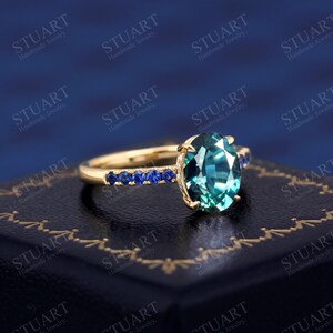 Pu&ograve; includere: Un anello d'oro con una grande pietra ovale di colore turchese circondata da una fila di piccole pietre blu.