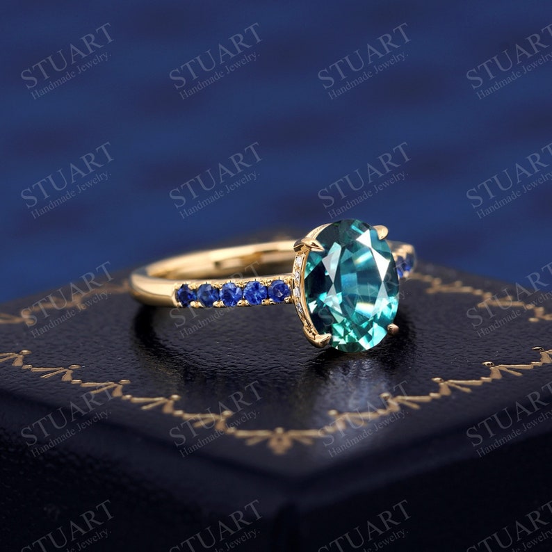Pu&ograve; includere: Un anello d'oro con una grande pietra ovale di colore turchese circondata da una fila di piccole pietre blu.