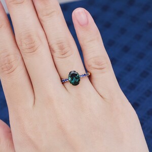 Puede incluir: Un anillo de oro con una piedra ovalada verde rodeada por una banda de piedras azules.
