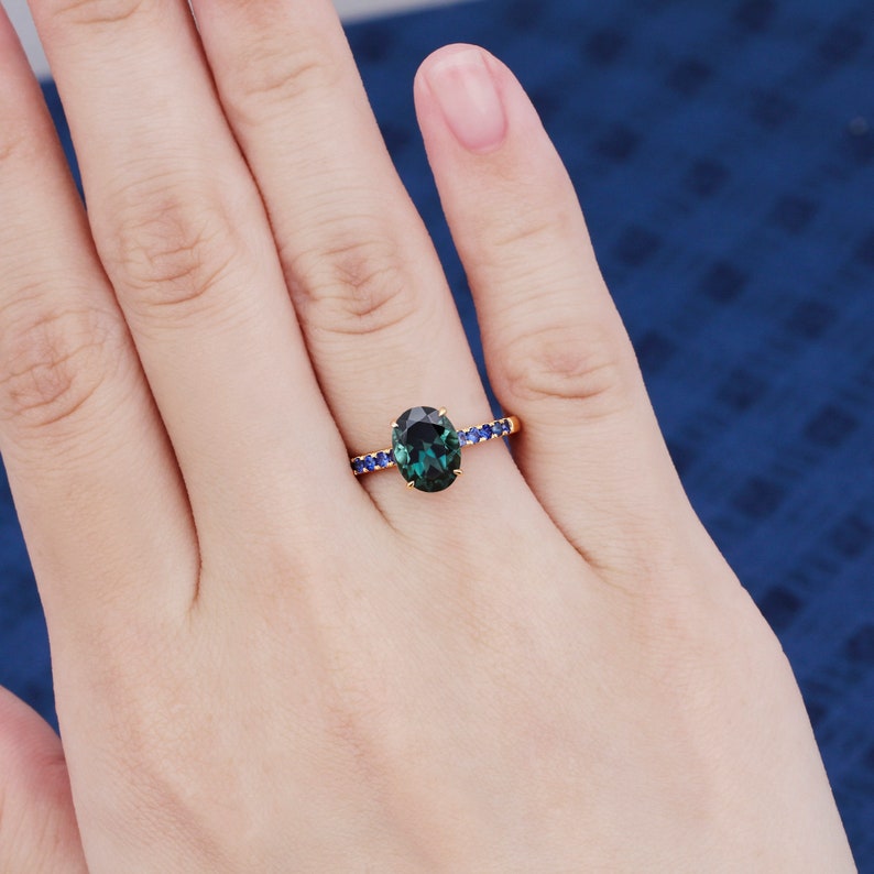 Puede incluir: Un anillo de oro con una piedra ovalada verde rodeada por una banda de piedras azules.