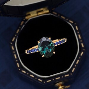 Puede incluir: Un anillo de oro con una gran piedra preciosa ovalada verde rodeada de peque&ntilde;as piedras azules.
