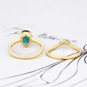 Op de afbeelding: Een gouden ring met een peervormige turquoise edelsteen en kleinere groene edelstenen op de band.