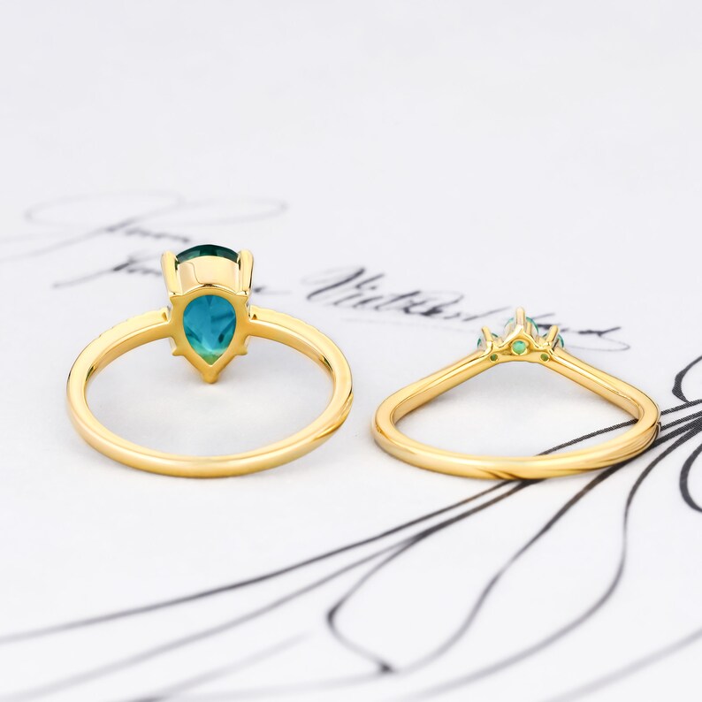 Op de afbeelding: Een gouden ring met een peervormige turquoise edelsteen en kleinere groene edelstenen op de band.