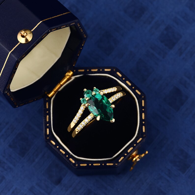 Op de afbeelding: Een gouden ring met een peervormige smaragd, omringd door kleinere smaragden en diamanten. De ring ligt in een blauwe fluwelen ringdoos.