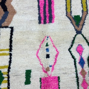 Peut inclure: Un tapis blanc avec un motif g&eacute;om&eacute;trique en noir, marron, rose, vert, jaune et bleu. Le tapis a une texture tiss&eacute;e &agrave; la main.