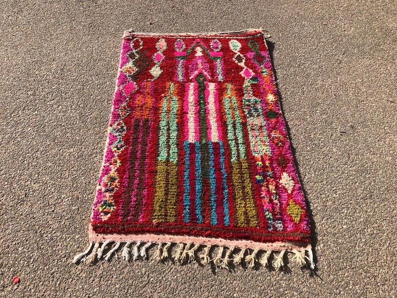 Puede incluir: Una alfombra marroqu&iacute; colorida con un patr&oacute;n geom&eacute;trico en tonos de rosa, rojo, verde, azul y marr&oacute;n. La alfombra tiene un borde de flecos y est&aacute; hecha de lana.